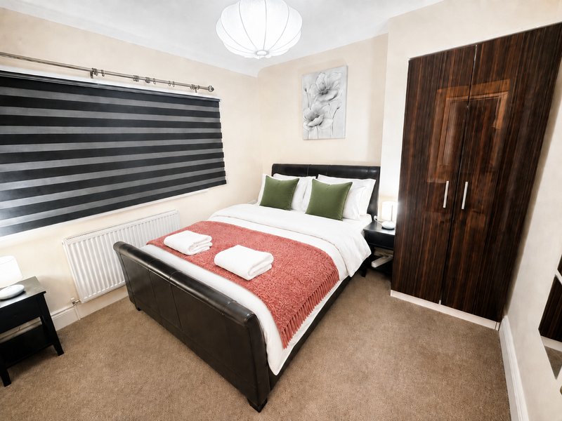 Modern bedroom with double bed, red throw, green cushions, wooden wardrobe and striped blinds