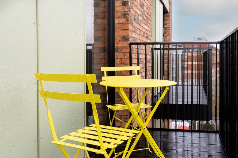 Bright yellow folding chairs and table on covered balcony with brick chimney and black railings