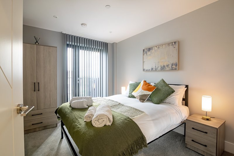 Modern bedroom with double bed, green bedding, wooden wardrobe and bedside lamp