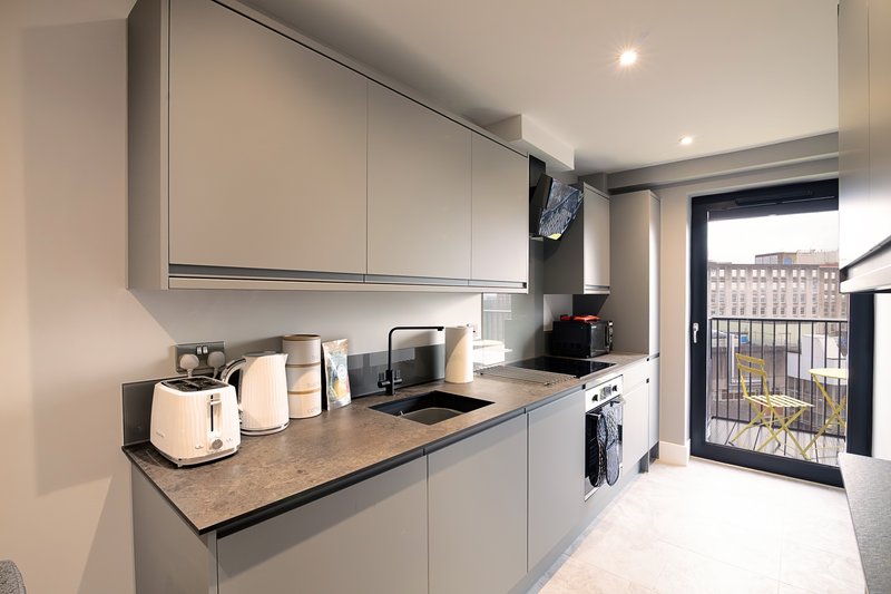 Modern kitchen with white cabinetry, stone countertop, kettle, and glass balcony doors