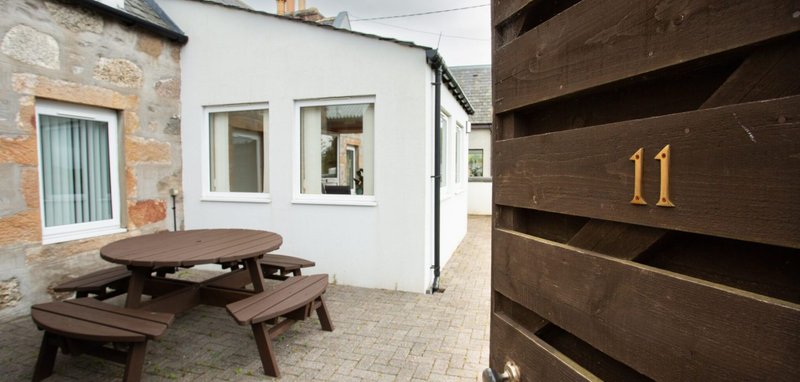 Exterior patio area with wooden picnic table and brown wooden fence showing house number