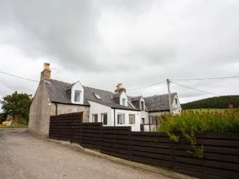 Stone and white-painted countryside cottage with dark fence and driveway