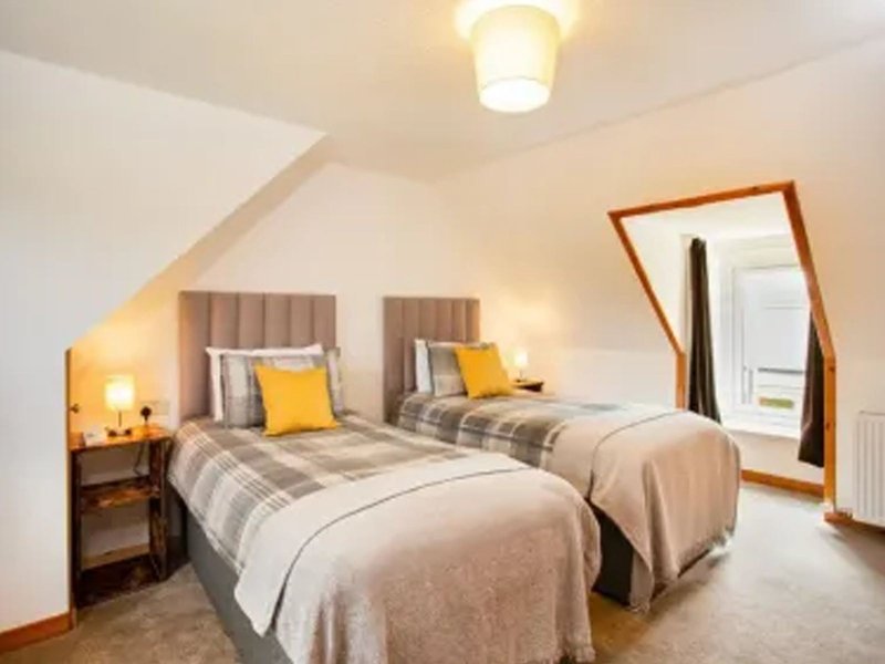 Bright attic bedroom with two single beds, upholstered headboards, yellow cushions, wooden mirror and ceiling light