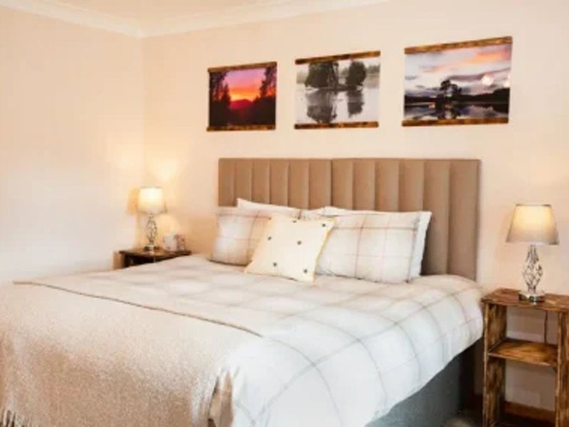 Bedroom with upholstered headboard, double bed, bedside lamps and framed landscape artwork