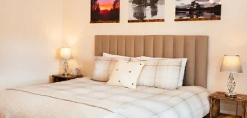 Bedroom with upholstered headboard, white bedding, decorative pillows, and framed landscape prints