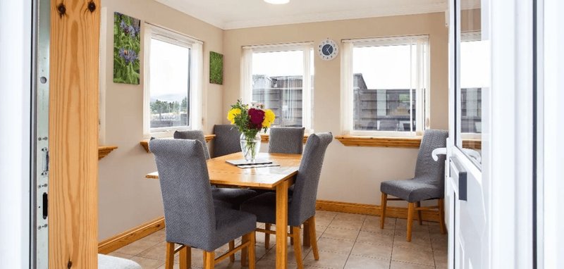 Bright dining area with wooden table, grey chairs, large windows and city views