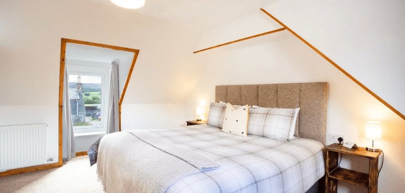 Bright attic bedroom with double bed, upholstered headboard, wooden beams and window