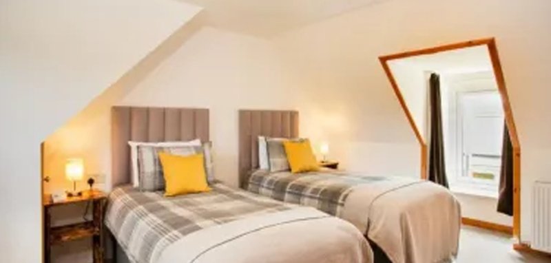 Twin bedroom with two single beds, upholstered headboards, plaid bedding, wooden mirror and bedside lamps