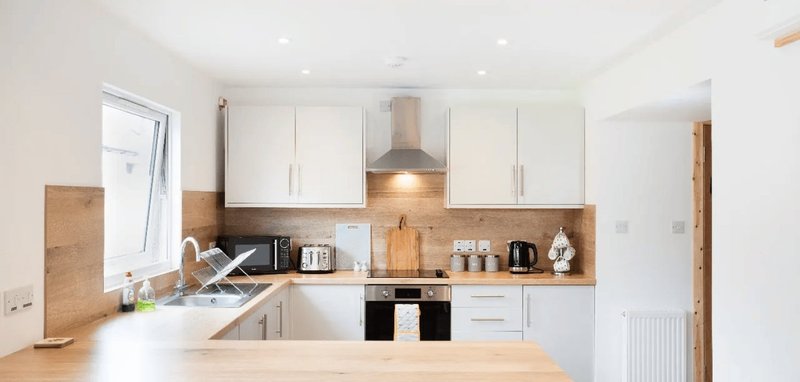 Modern kitchen with white cabinetry, wooden countertops, black oven and extractor hood