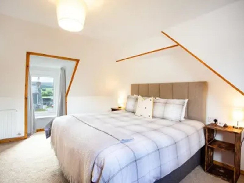 Bright attic bedroom with double bed, wooden nightstand, mirror and sloped ceiling beams
