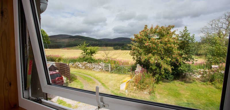 Rural landscape view through window: green fields, mountains, trees and country garden