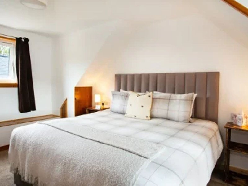 Bright bedroom with upholstered headboard, white bedding, wooden nightstands, and window with dark curtains