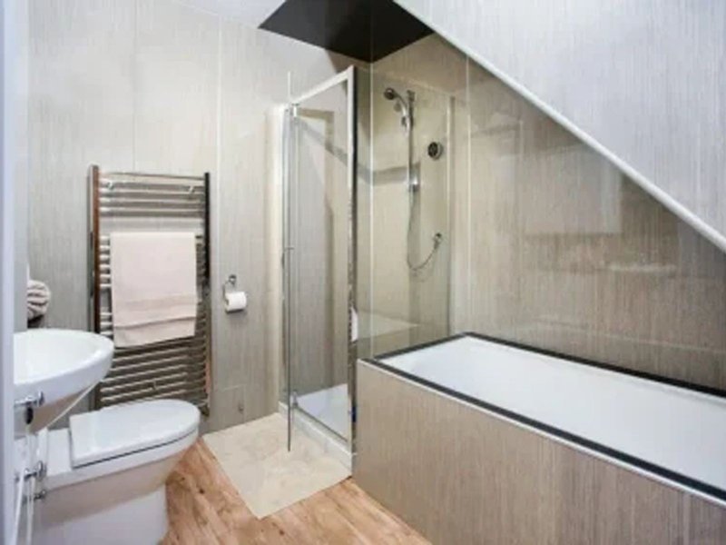 Modern bathroom with walk-in shower, heated towel rail, toilet and wooden flooring under sloped ceiling