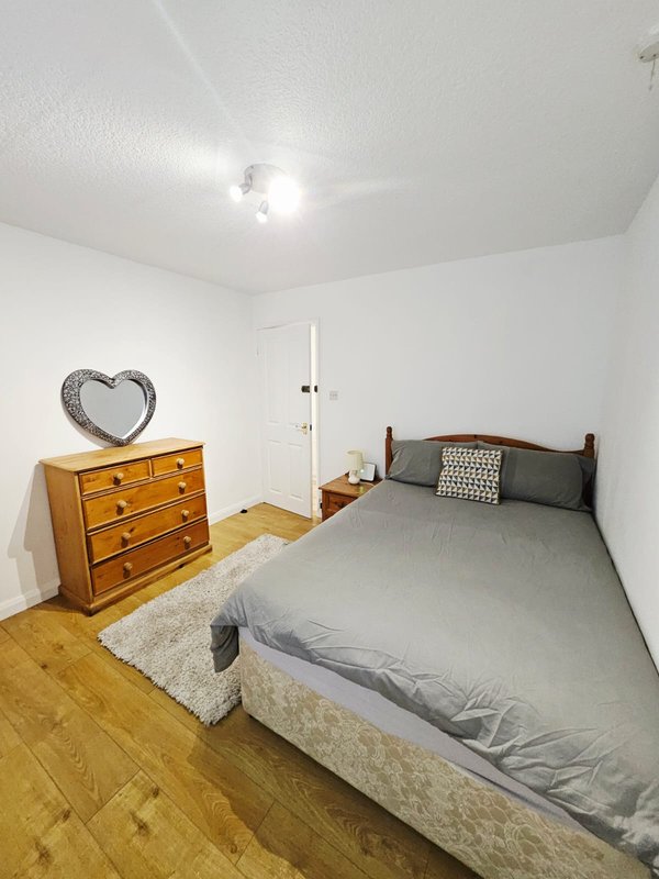 Modest bedroom with double bed, wooden chest of drawers, wooden floor and white walls