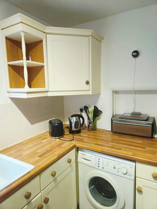 Compact kitchen with cream cabinetry, wooden countertop, white washing machine and appliances