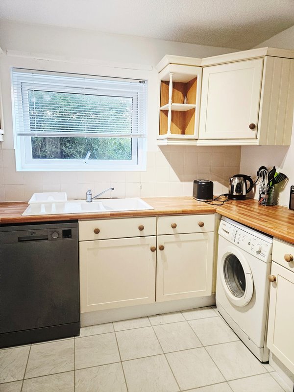 Kitchen with cream cabinets, wooden worktops, dishwasher, washing machine and window