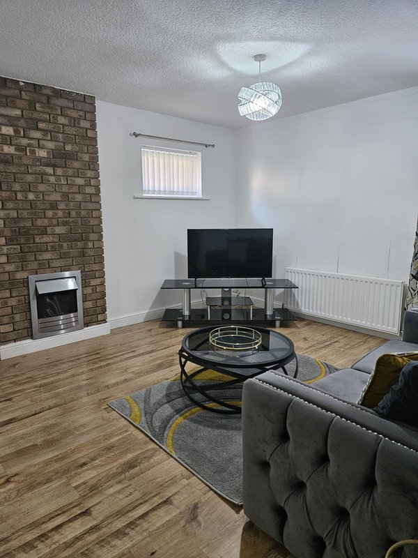 Living room with grey sofa, TV on stand, brick fireplace, wooden flooring and pendant light