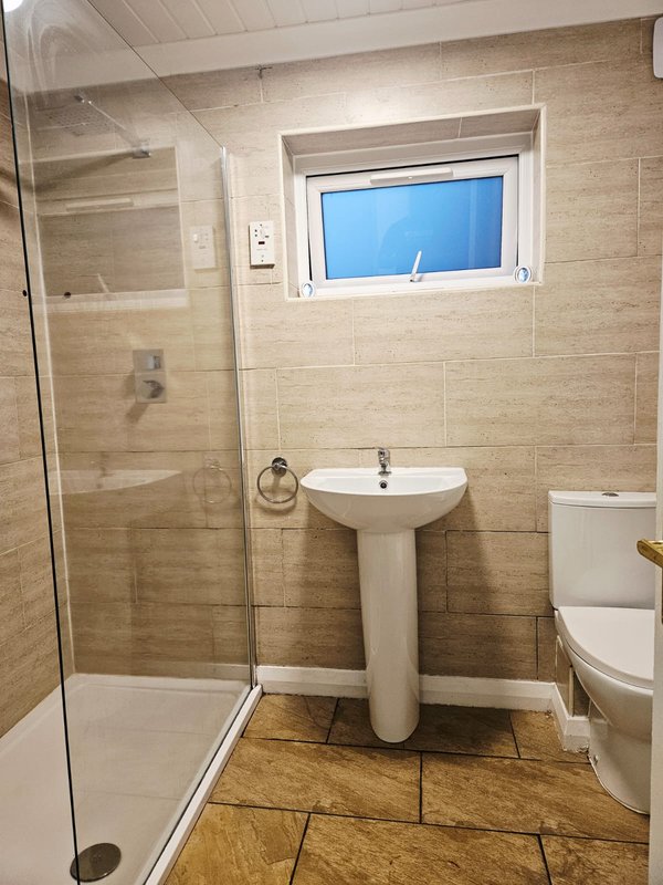 Modern bathroom with shower cubicle, pedestal sink, toilet and small window
