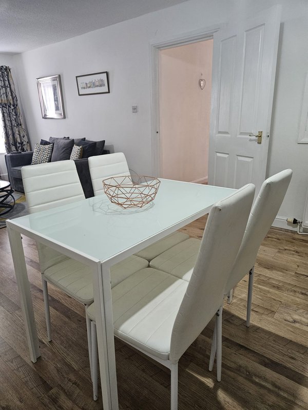 Modern dining area with white table, cream chairs, and open-plan living space beyond