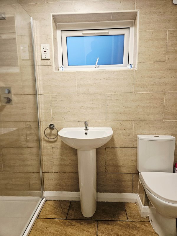 Modern bathroom with pedestal sink, toilet, tiled walls and window