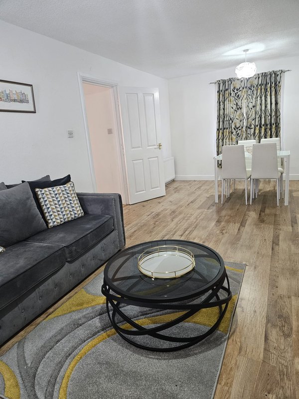 Open-plan living and dining area with grey sofa, round coffee table, wooden flooring and patterned curtains