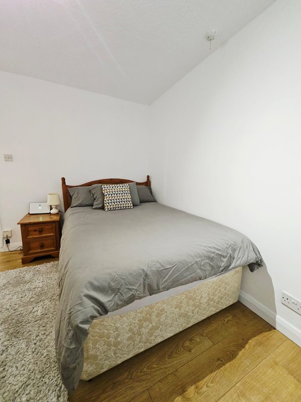 Bedroom with double bed, wooden bedside table, white walls and wooden floor