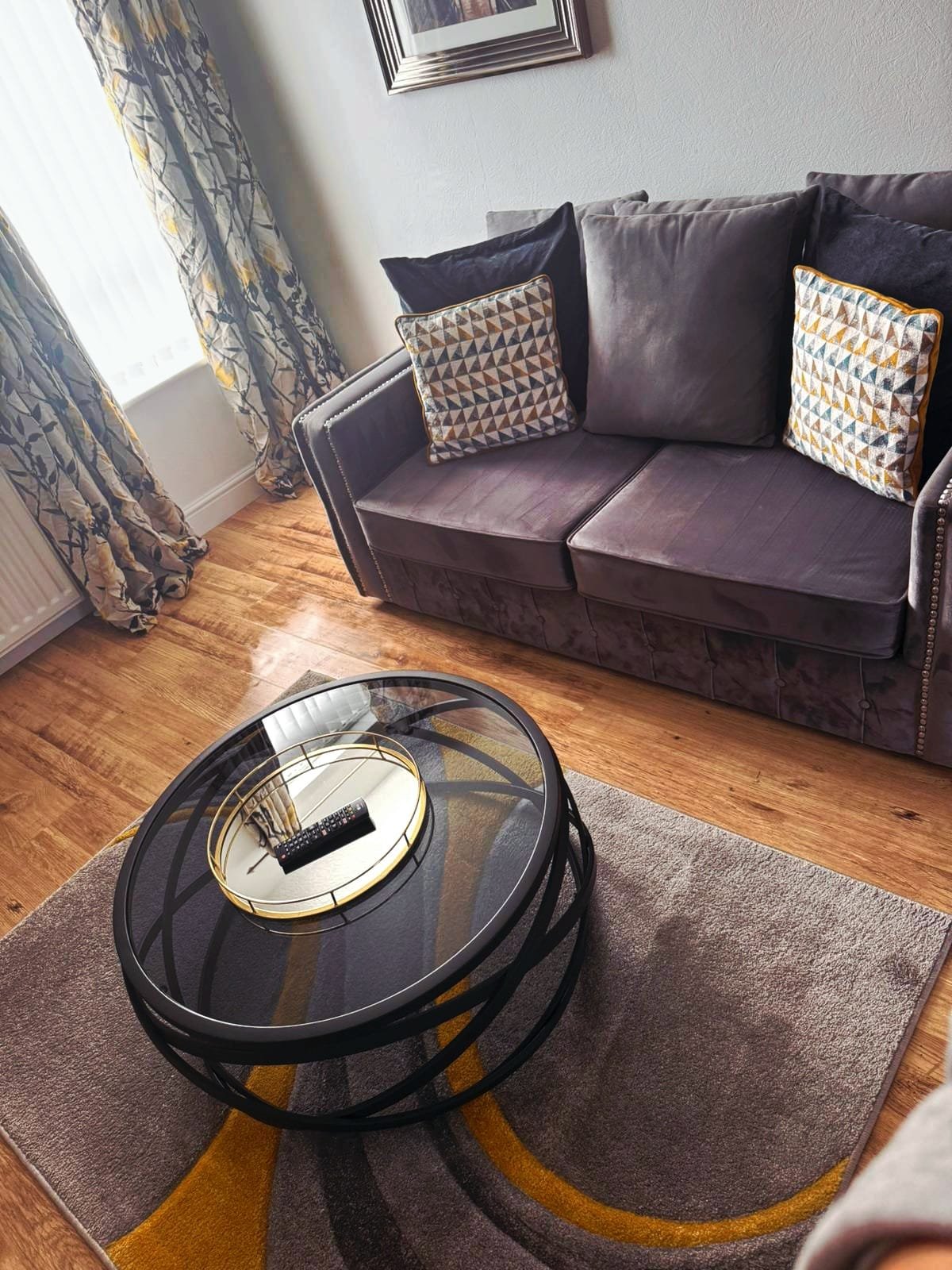 Living room with dark sofa, patterned cushions, round glass coffee table, wooden flooring and patterned rug