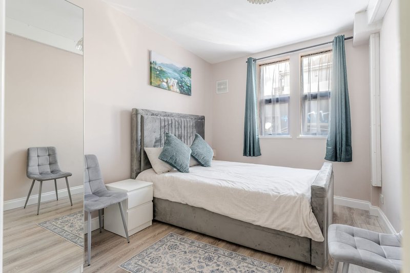 Bright bedroom with single bed, grey upholstered chair, wooden floor and large windows with curtains
