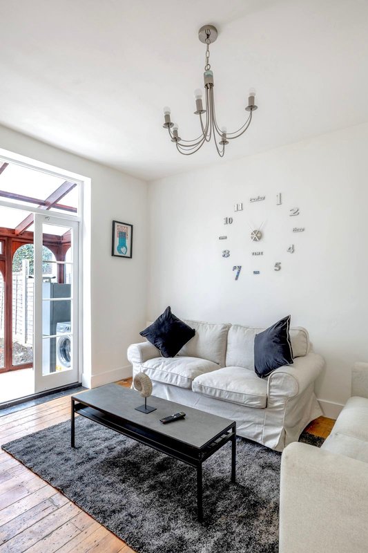 Bright living room with cream sofa, black coffee table, chandelier, and wall clock