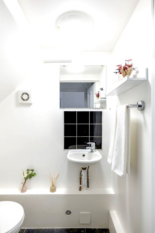 Clean modern bathroom with white walls, pedestal sink, mirror, and black tile accents