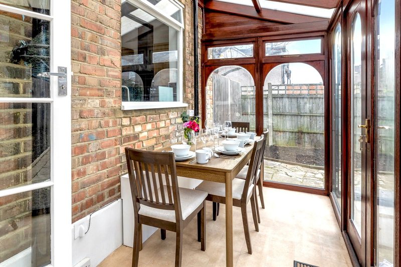 Brick conservatory with wooden dining table, chairs, and large glass doors overlooking garden