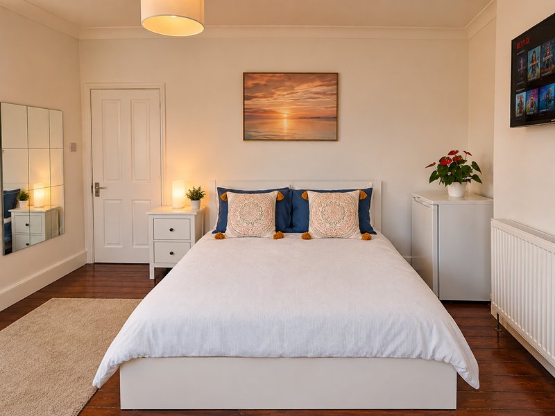 Bright bedroom with double bed, white bedding, blue and patterned pillows, wooden floor and wall art