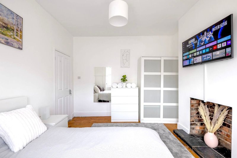 Bright modern bedroom with double bed, white wardrobe, mounted TV, and wooden floor
