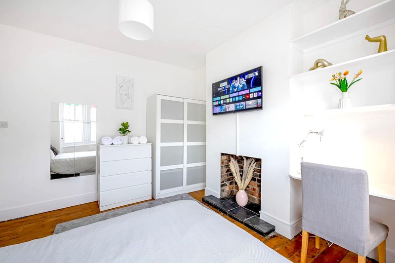Bright bedroom with white walls, wooden floor, bed, dresser, and wall-mounted TV