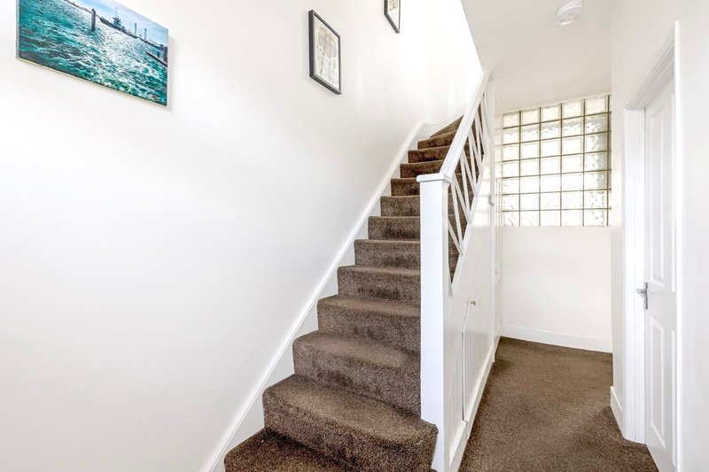Staircase with brown carpet, white walls, and framed artwork, leading to upper floor