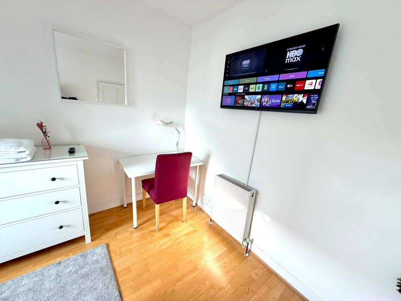 Bedroom with wall-mounted TV, white desk, red chair, mirror, wooden floor and radiator