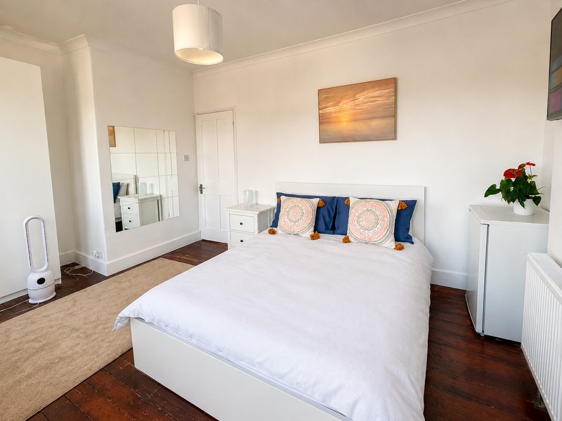 Bright bedroom with white double bed, blue and orange cushions, wooden floor and ceiling light