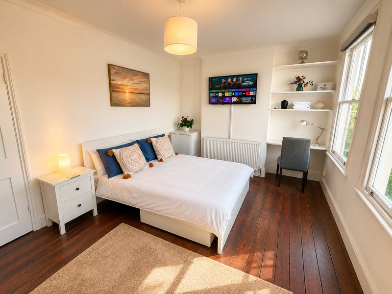 Bright bedroom with double bed, white nightstand, wall-mounted TV, and built-in shelving