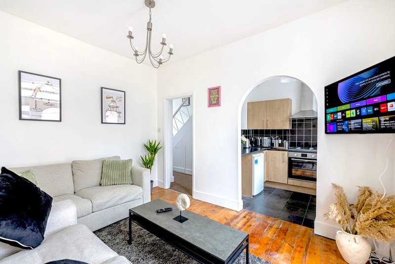 Open-plan living room with beige sofa, black coffee table, kitchenette, and wall-mounted television