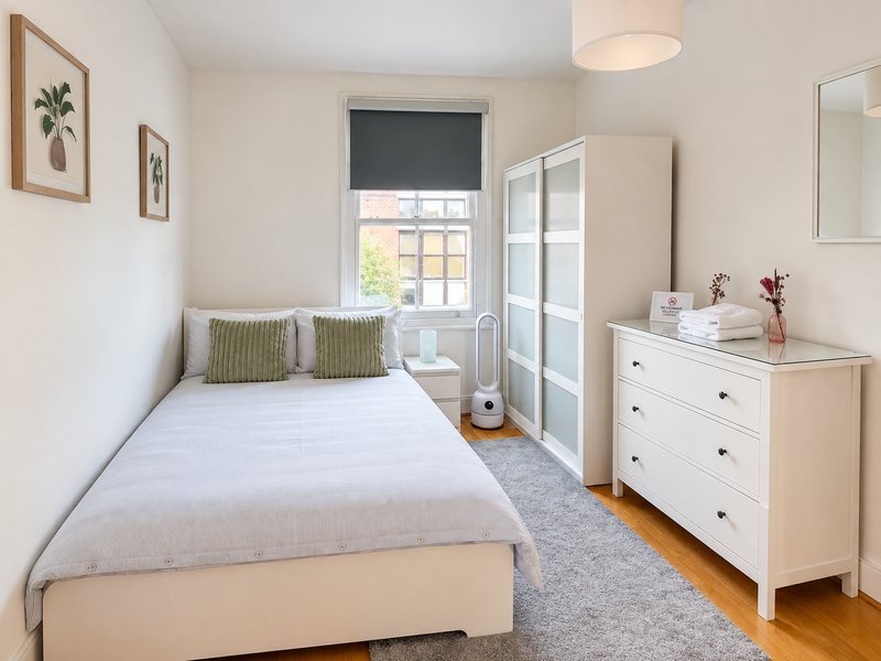 Bright bedroom with single bed, white dresser, window with blind, and framed wall art