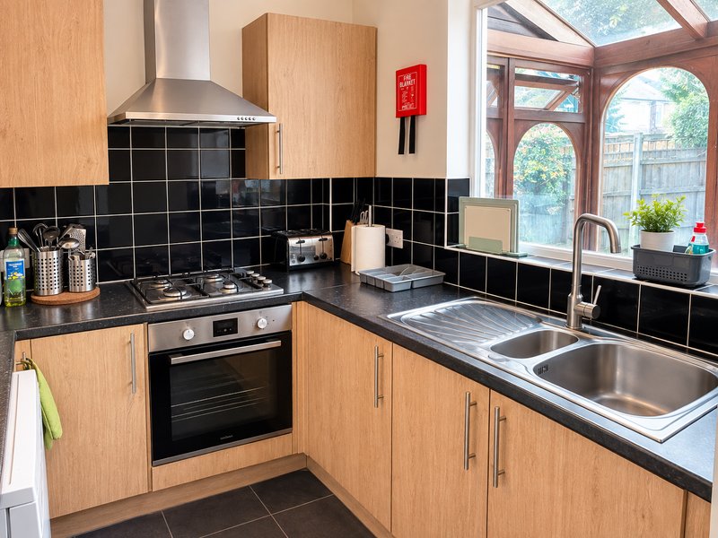 Modern kitchen with wooden cabinets, black tile backsplash, stainless steel appliances and sink