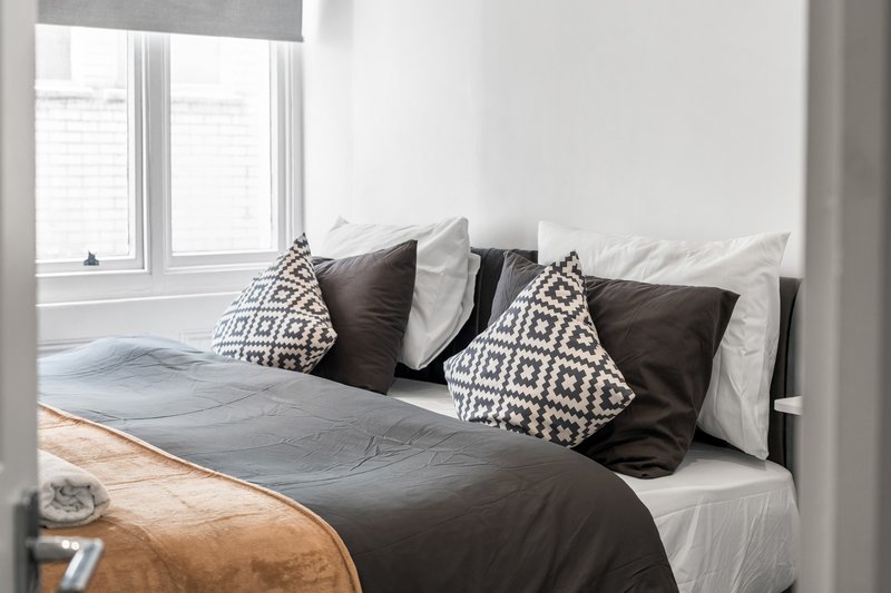 Modern bedroom with double bed, dark bedding, patterned cushions and large windows