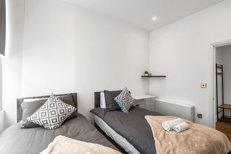 Modern bedroom with double bed, patterned cushions, white walls and wooden flooring