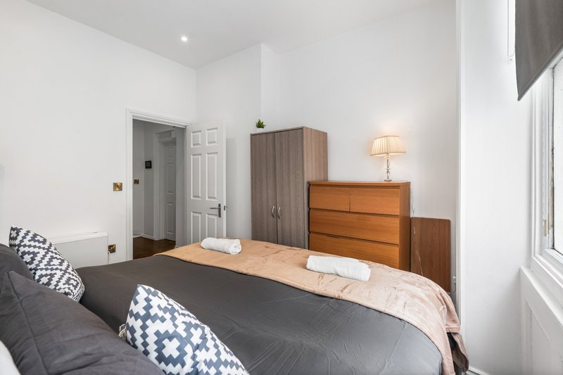 Bedroom with double bed, wooden dresser, wardrobe, bedside lamp and white walls