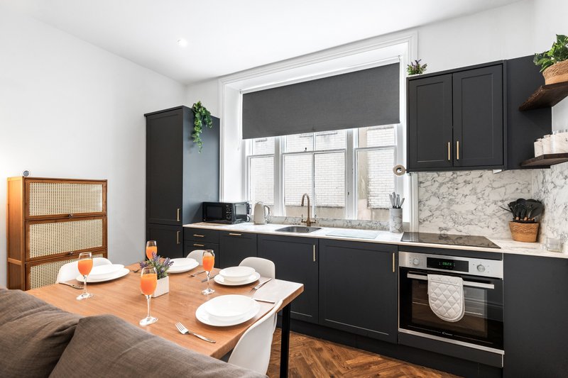 Modern kitchen with black cabinetry, marble backsplash, and wooden dining table set for two