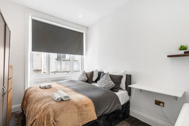 Modern bedroom with double bed, patterned cushions, window with city view, and wall-mounted shelf