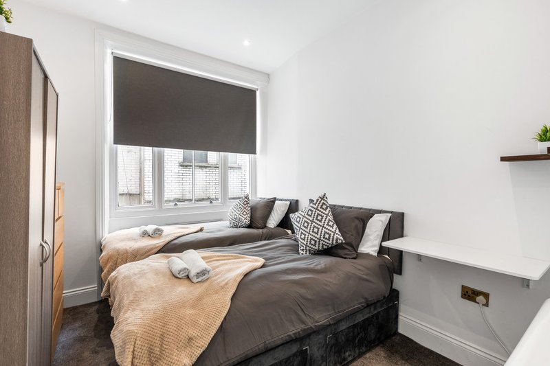 Bedroom with double bed, dark bedding, decorative pillows and window with roller blind