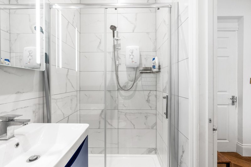 Modern bathroom with marble-effect tiles, walk-in shower enclosure, white sink vanity, and mirror