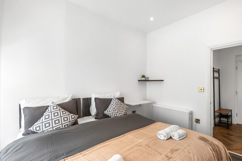 Modern bedroom with double bed, geometric cushions, wooden floor and white walls