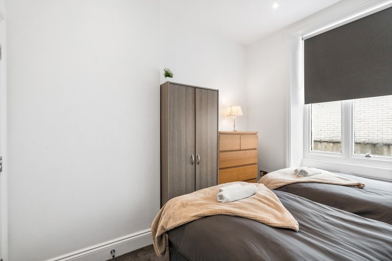 Bedroom with double bed, wooden wardrobe, bedside lamp and window with dark blind